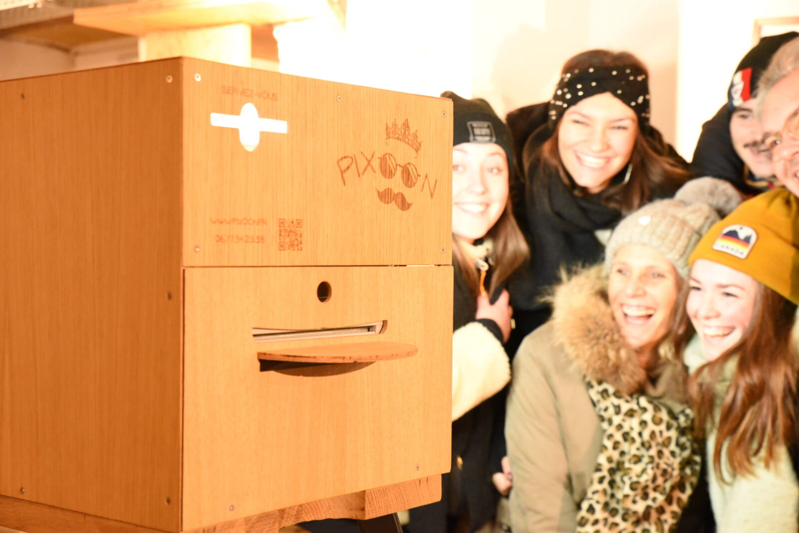 Un groupe d’amis rit à côté du photobooth Pixoon en bois, dont on voit la façade gravée