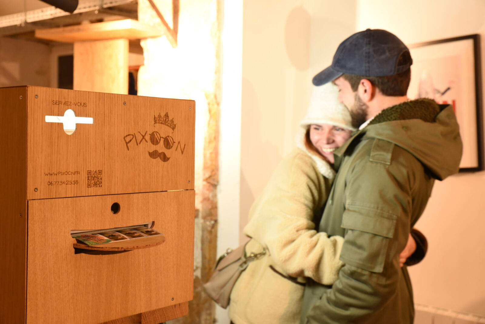Un couple enlacé devant le photobooth Pixoon en bois, sous une lumière chaude