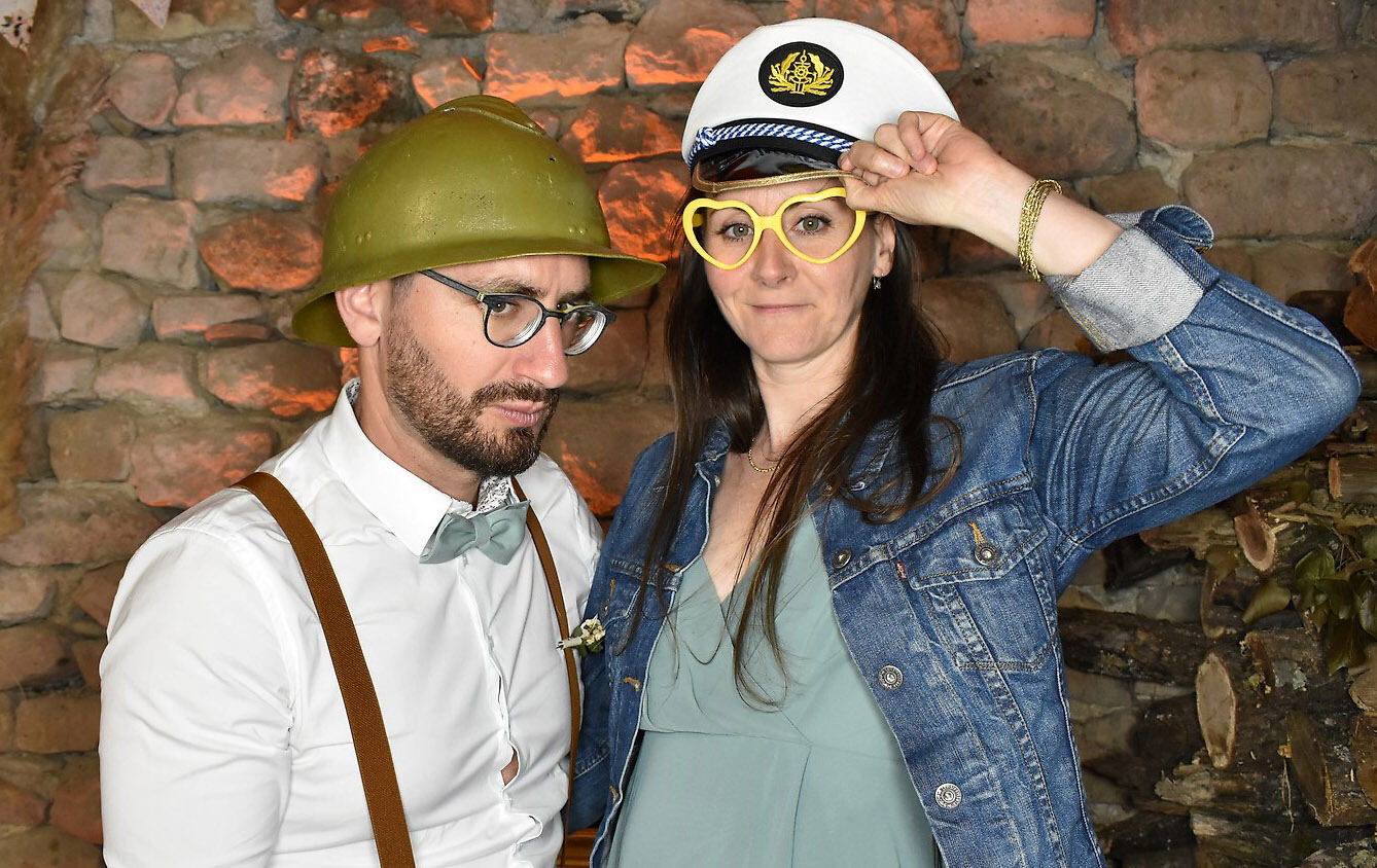 Deux invités posent devant un mur de pierre, l’un avec un casque vert, l’autre avec un chapeau blanc