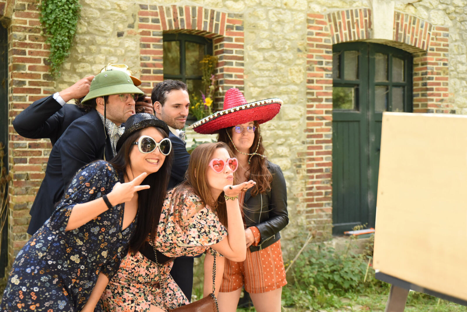 Quatre invités avec chapeaux et lunettes de soleil posent devant un bâtiment en brique