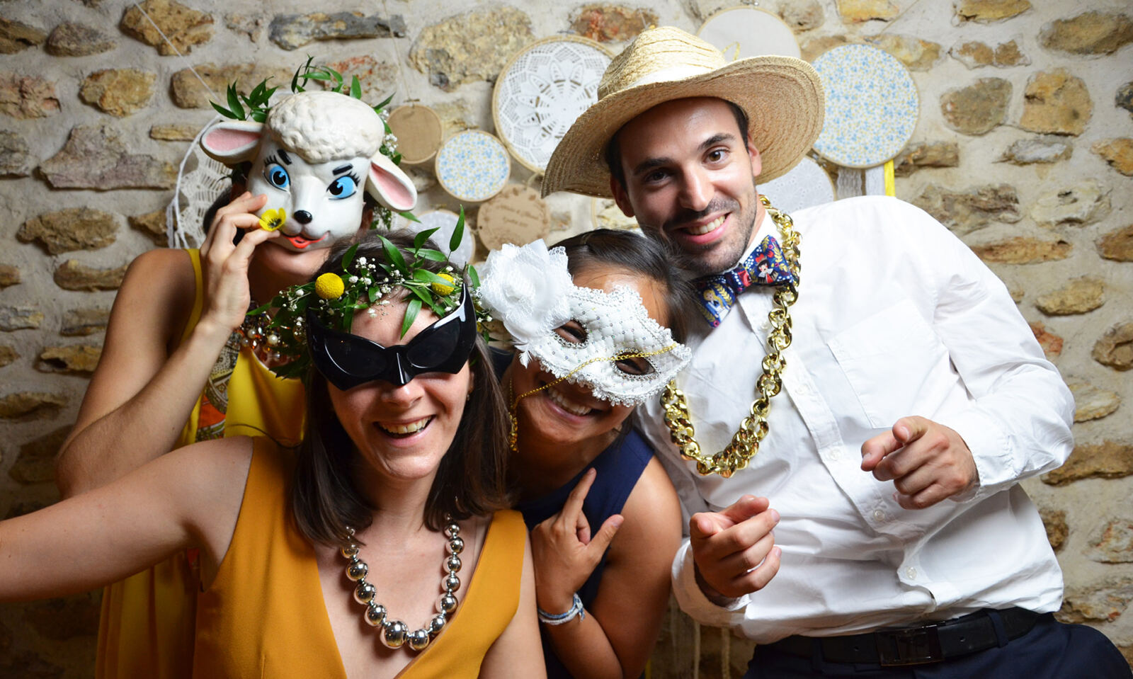 Trois invités avec masques et chapeau posent devant un mur de pierre