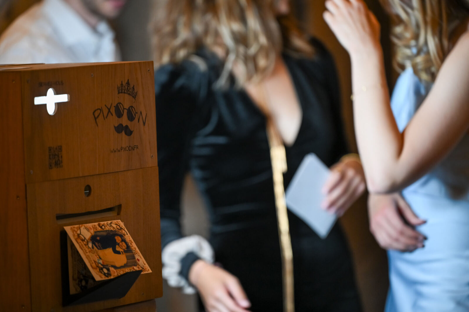 Un invité montre son tirage sorti du photobooth Pixoon en bois pendant une soirée